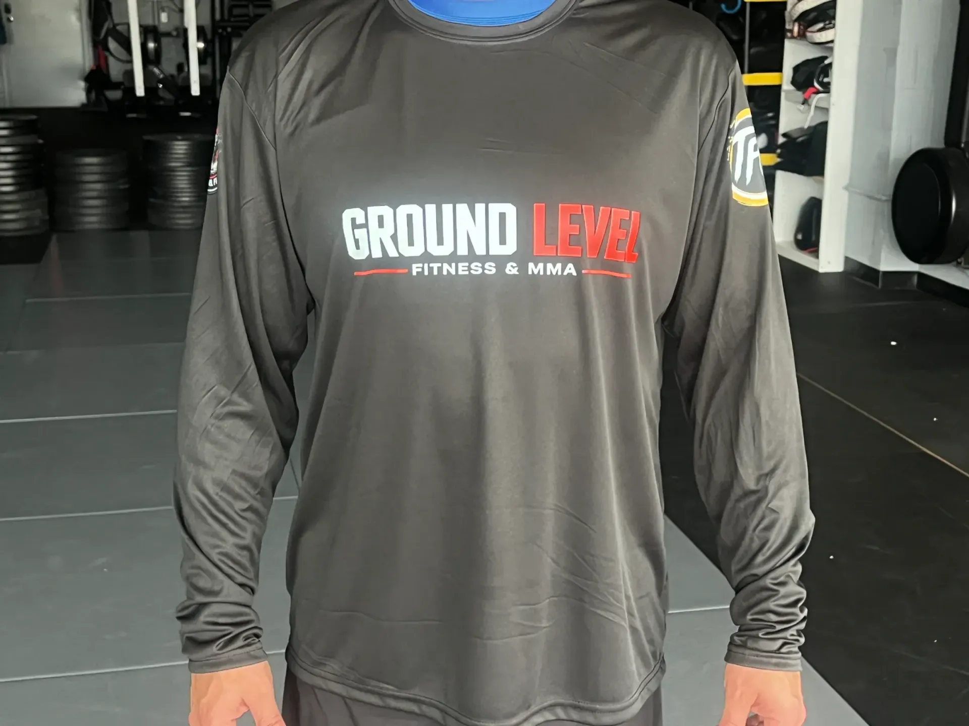 Gray long-sleeve athletic shirt with “GROUND LEVEL” logo, worn indoors in a gym.