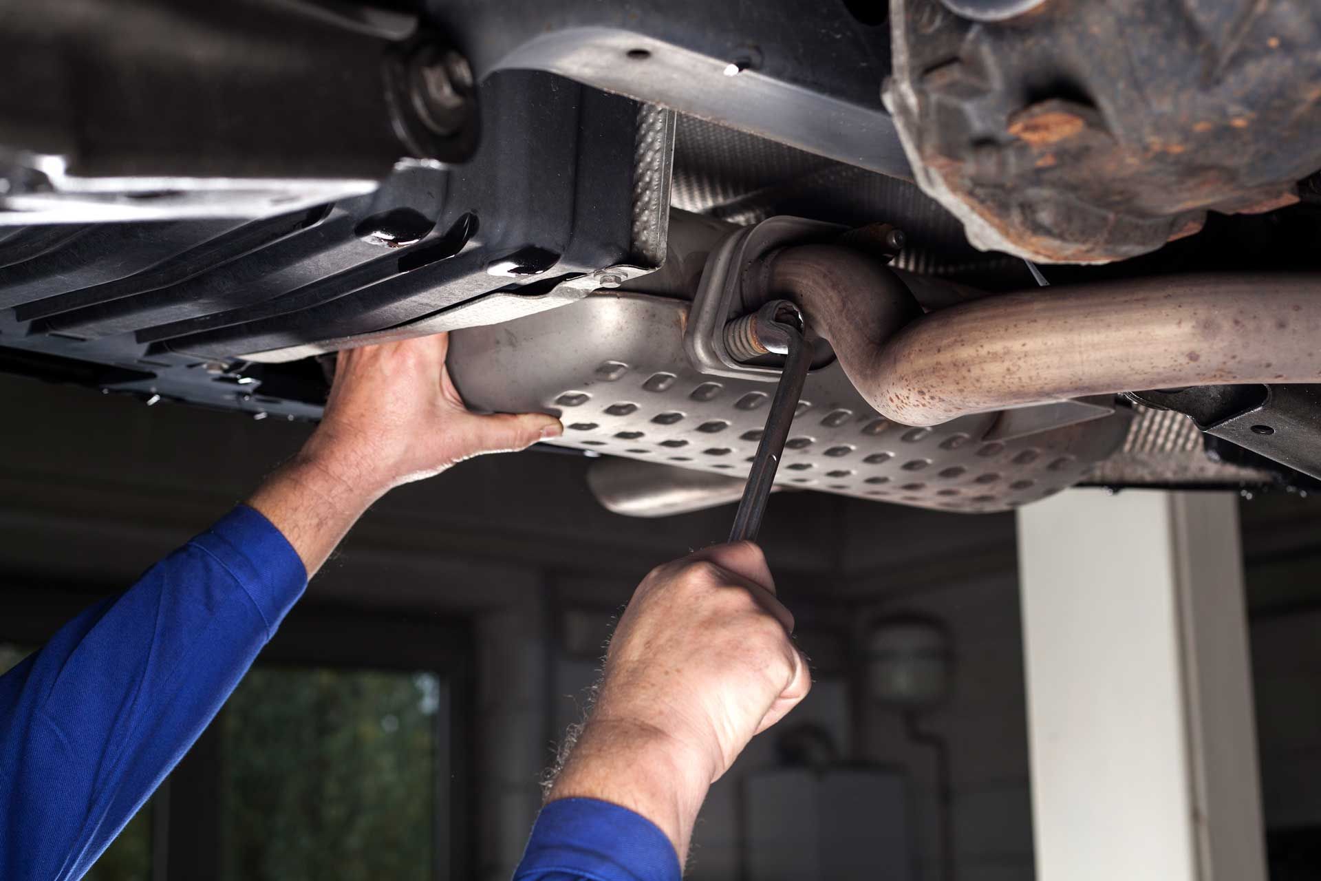 A man is working on the exhaust pipe of a car.