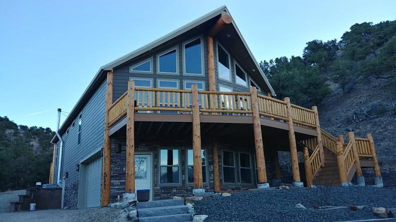 Wooden cabin with large deck and A-frame roof in a rocky hillside setting