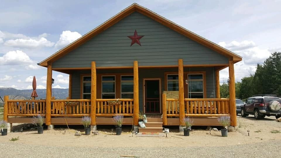Rustic wooden cabin with a porch and red star on the front, set on a gravel lot under cloudy skies