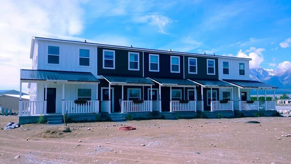 Row of two-story townhouses with porches under a blue sky on a sandy lot