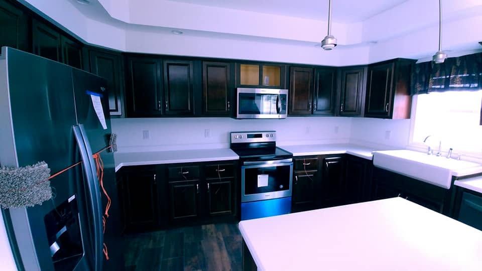 Modern kitchen with dark cabinets, stainless appliances, and a large white island under bright windows