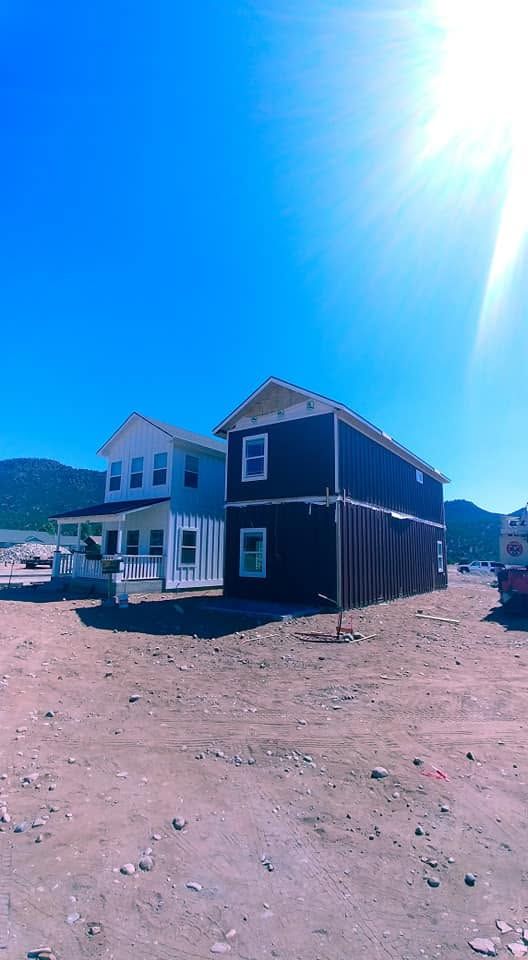 Two houses in a dry lot under a bright blue sky, with mountains in the distance.