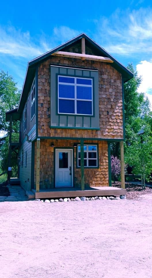 Two-story rustic wooden cabin with a large blue window and front door under a bright sky