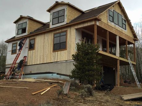 New house under construction with ladders and unfinished siding on a sloped lot