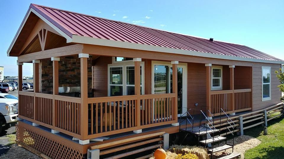 Tiny red-roofed cabin with a wooden porch and ramp on a sunny day