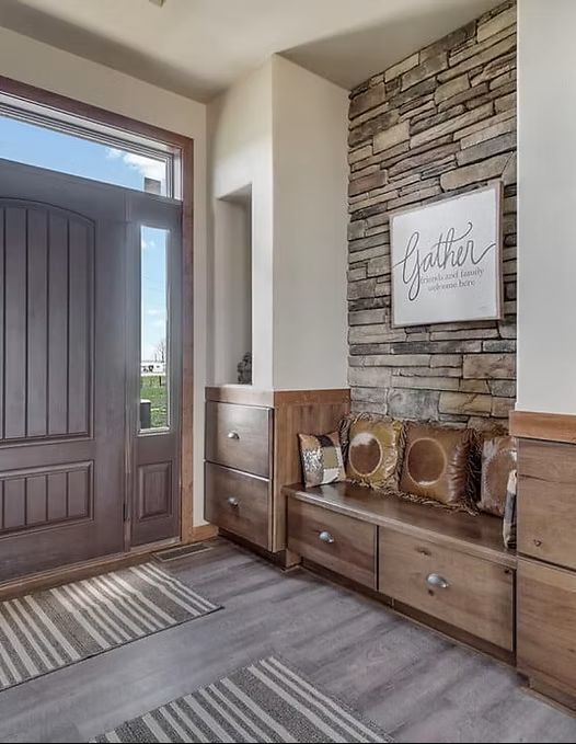 Modern entryway with wood front door, stone accent wall, console table, and striped rugs