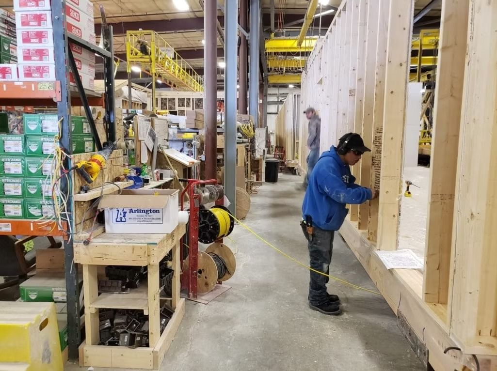 Worker in blue jacket measuring a wooden wall in a warehouse aisle