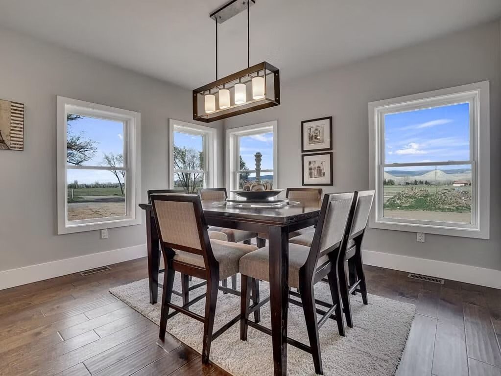 Modern dining room with dark wood table, upholstered chairs, pendant light, and large windows overlooking open fields