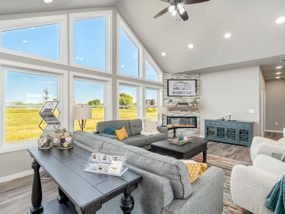 Bright modern living room with large windows, gray sectional, fireplace, and yellow accents