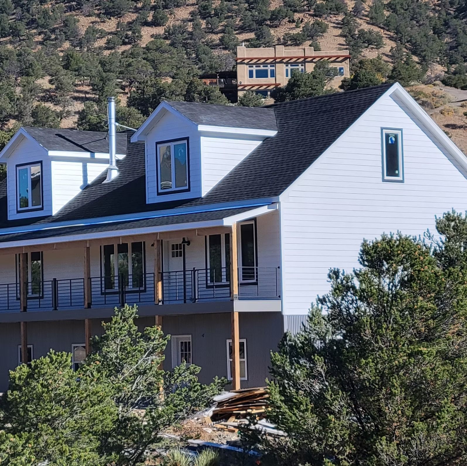 White two-story house with black roof and porch, set among trees on a hillside