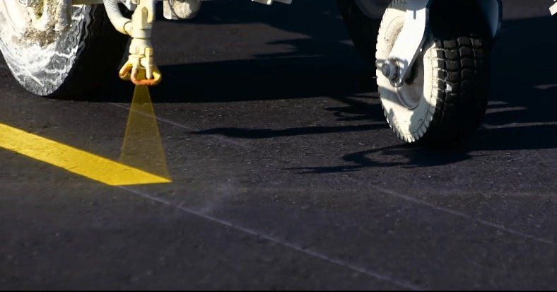 The first image is of an asphalt striping job being performed at a parking lot in Milwaukee. The second picture is of an asphalt professional sealcoating a parking lot in WIsconsin. The third image is of a large crack in an asphalt road that needs to be repaired.