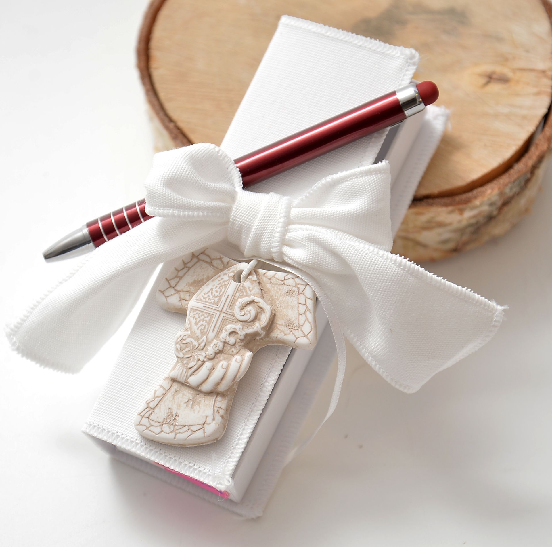 Quaderni con copertina bianca, legati con un fiocco bianco, una penna rossa e un ciondolo decorativo su una fetta di legno.