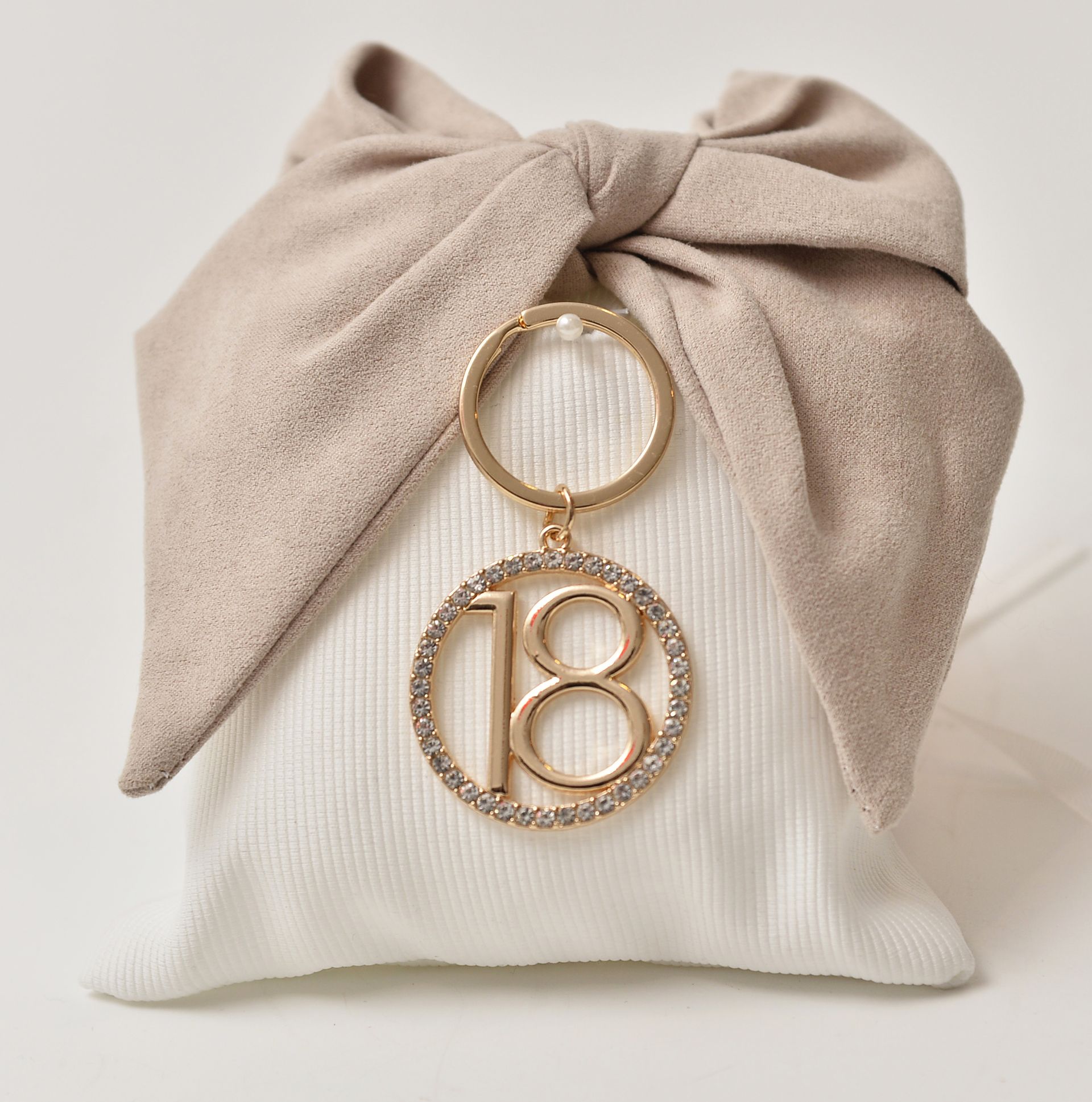 Fiocco beige annodato su una pochette bianca, portachiavi dorato con ciondolo 