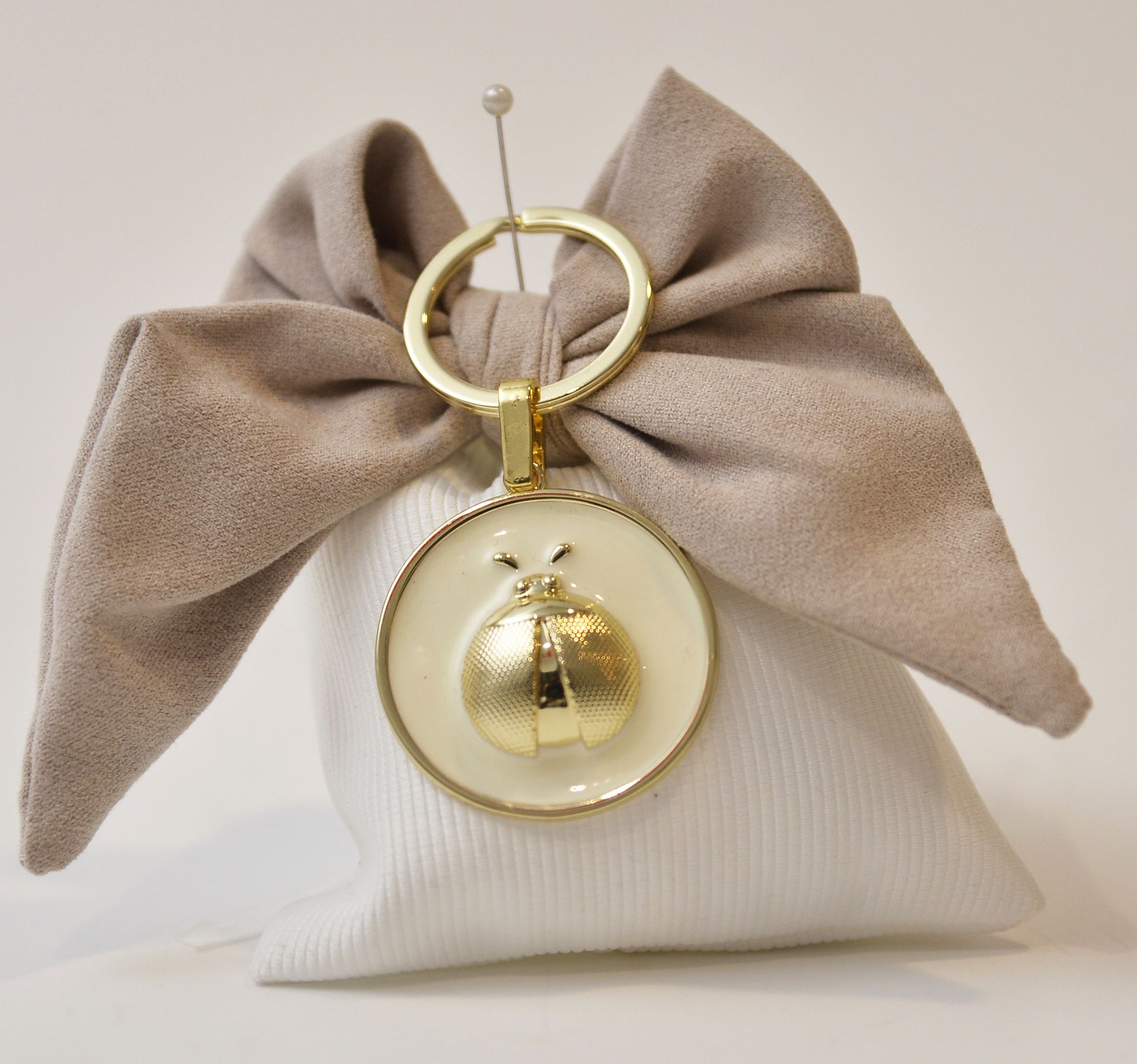 Borsa in tessuto bianco e beige con fiocco color cuoio, anello dorato e ciondolo a forma di coccinella dorata.