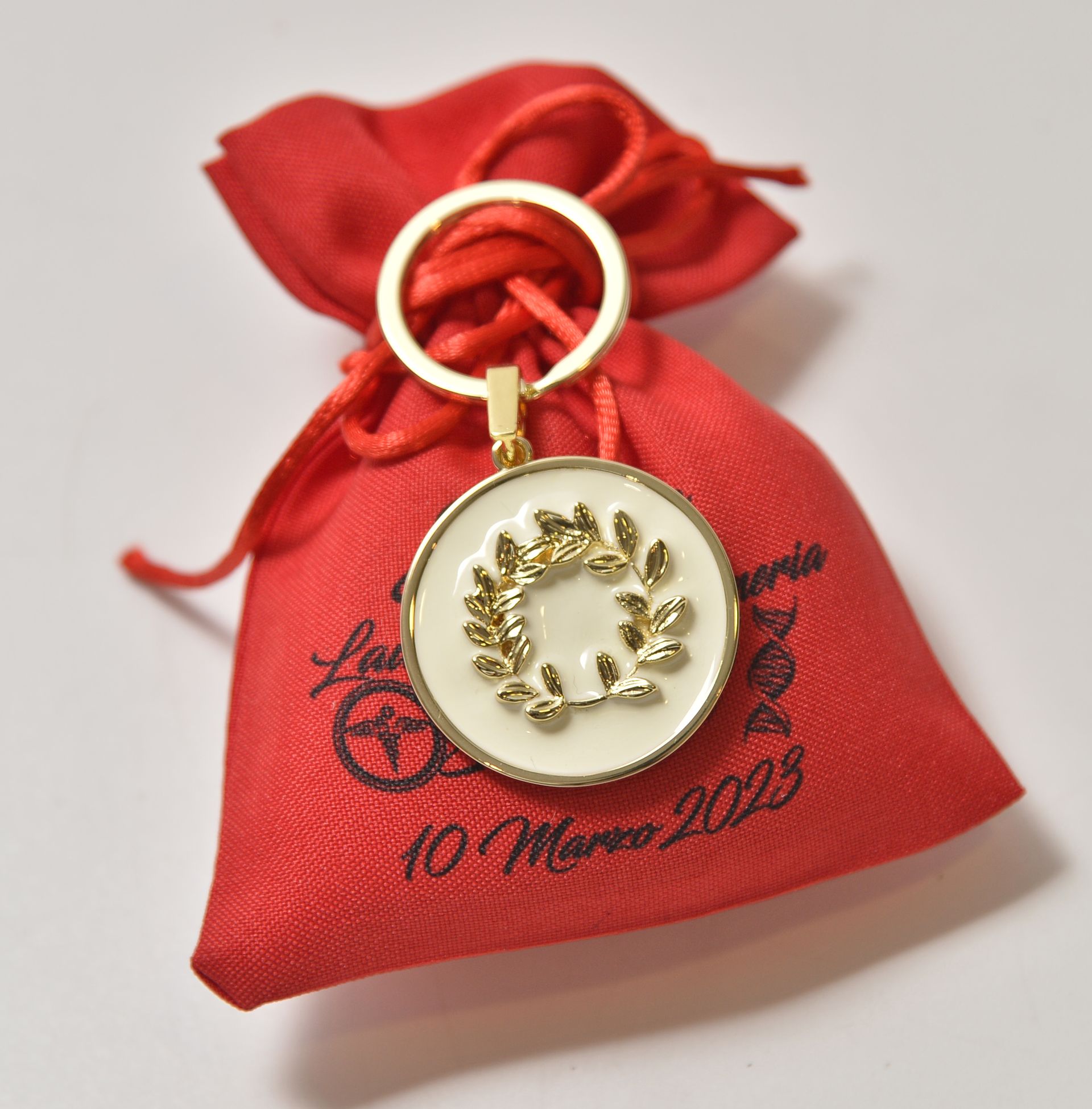 Portachiavi color oro con ciondolo a forma di corona su sacchetto rosso con coulisse, probabilmente un regalino per una festa.