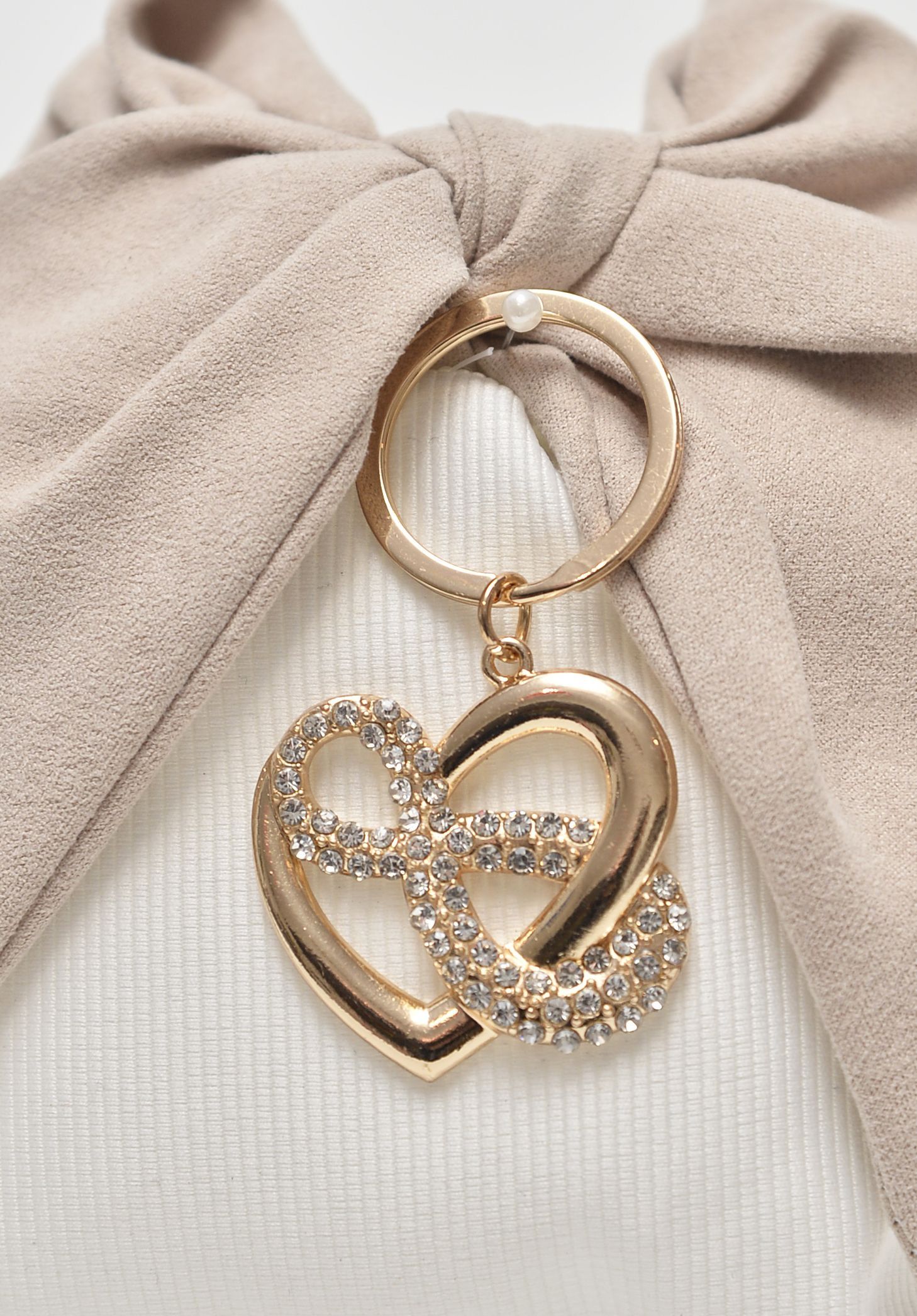 Ciondolo a forma di cuore in oro con strass appeso a un anello dorato con fiocco beige.