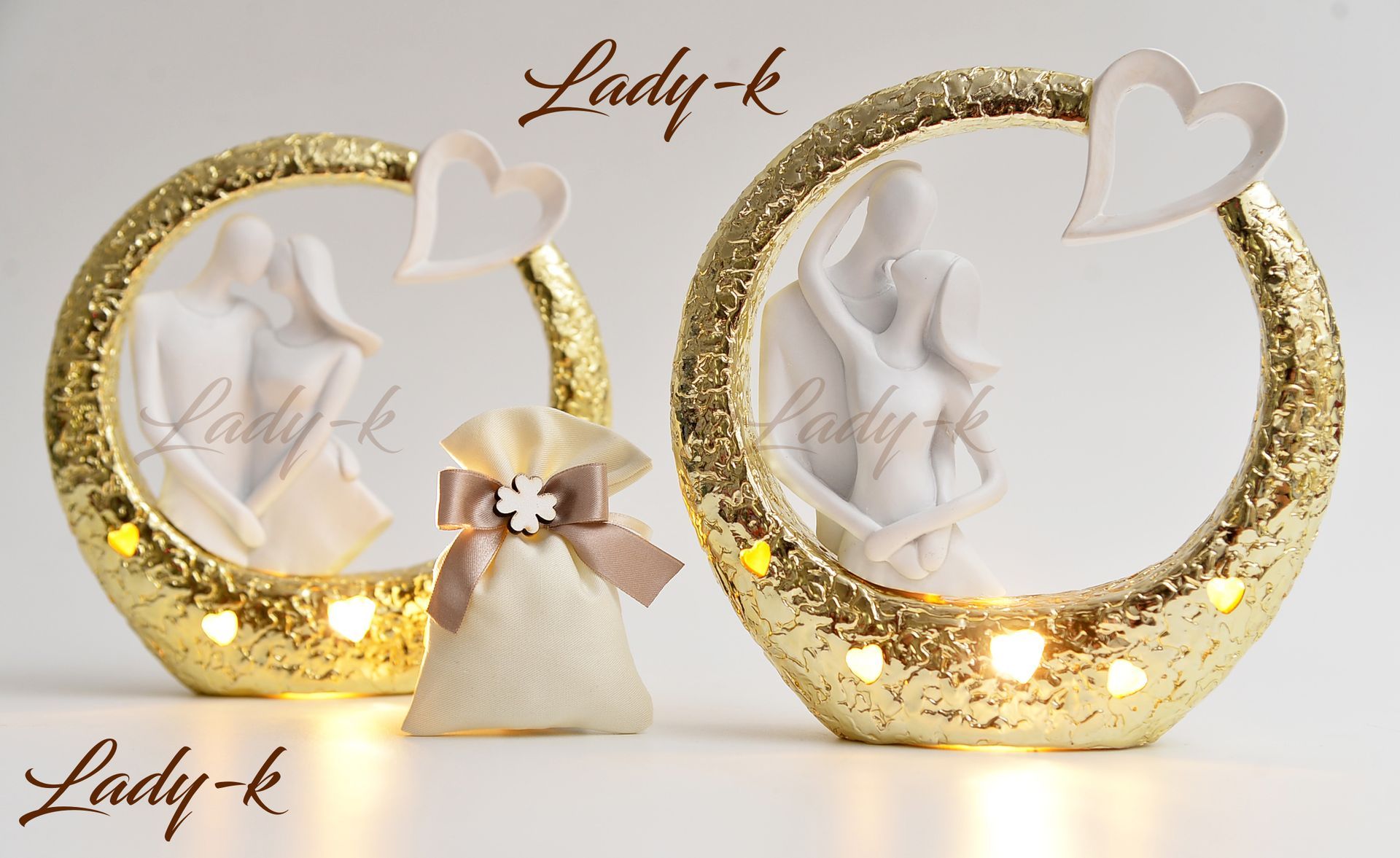 Due decorazioni circolari dorate e scintillanti con figure illuminate, accenti a forma di cuore e una piccola borsa regalo.
