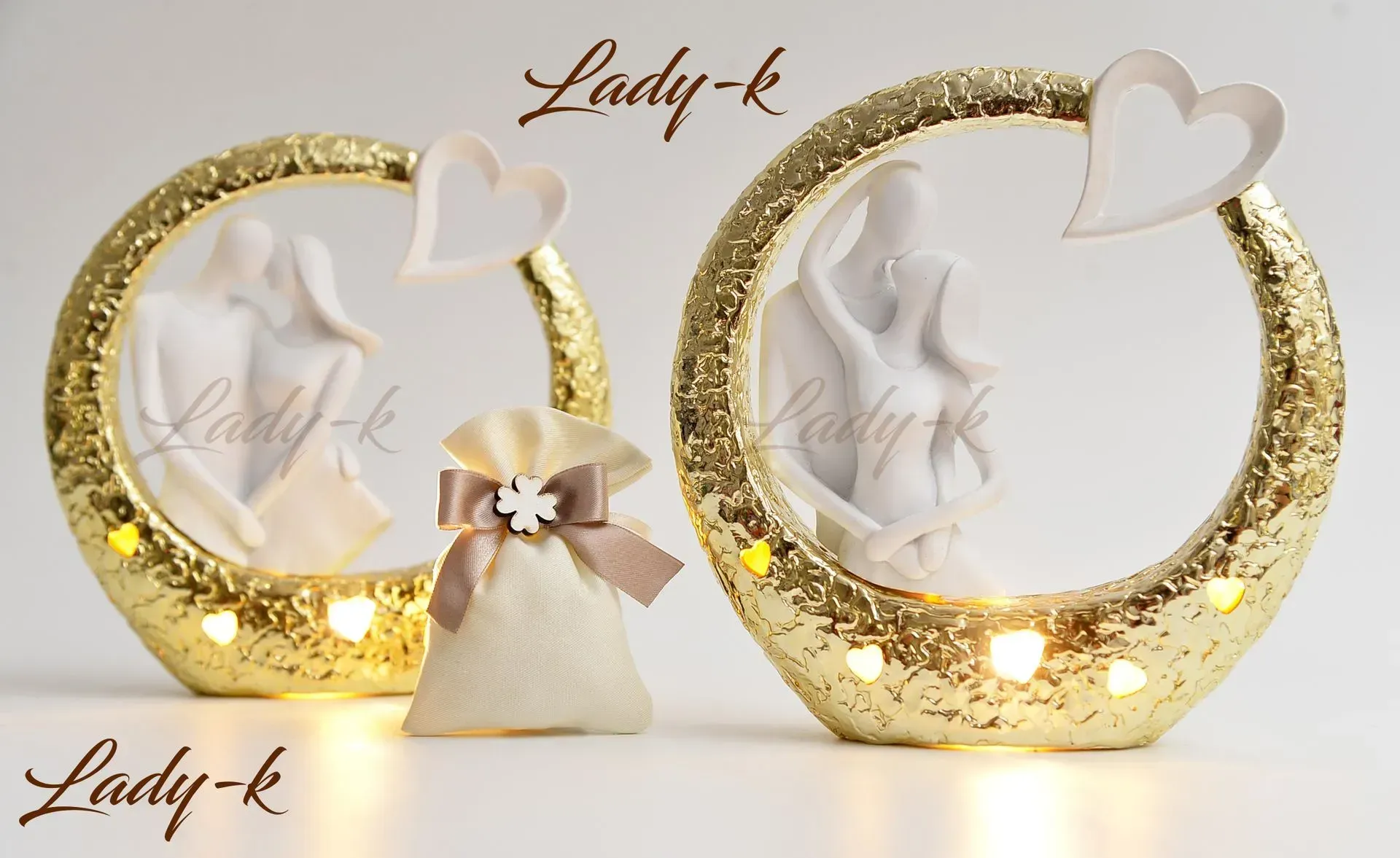 Due decorazioni luminose circolari dorate scintillanti con statuette di coppia e decorazioni a forma di cuore, e una piccola borsa regalo.