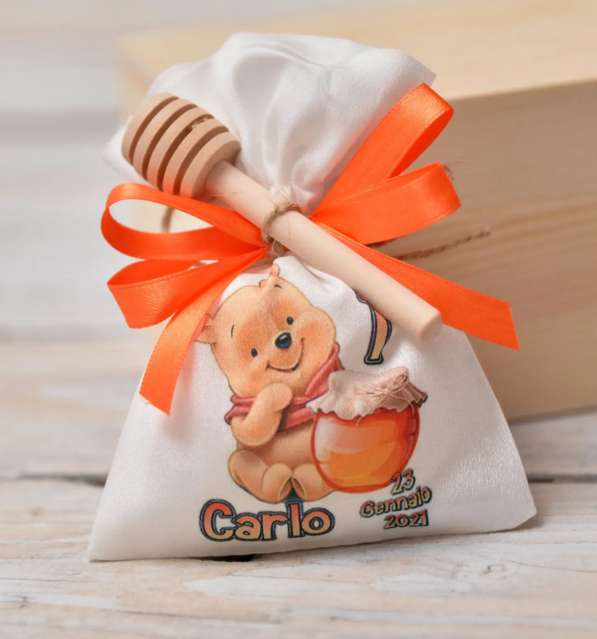 Sacchetto bianco per bomboniere con Winnie the Pooh, legato con un nastro arancione, un mestolo per il miele e il nome