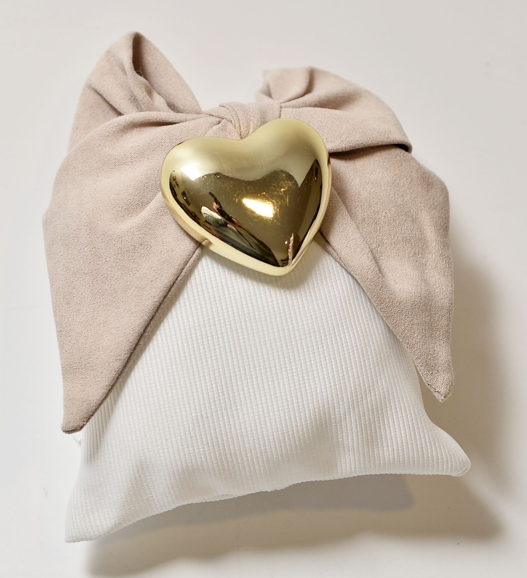 Fiocco in tessuto color cuoio con chiusura a forma di cuore dorato su cuscino bianco.
