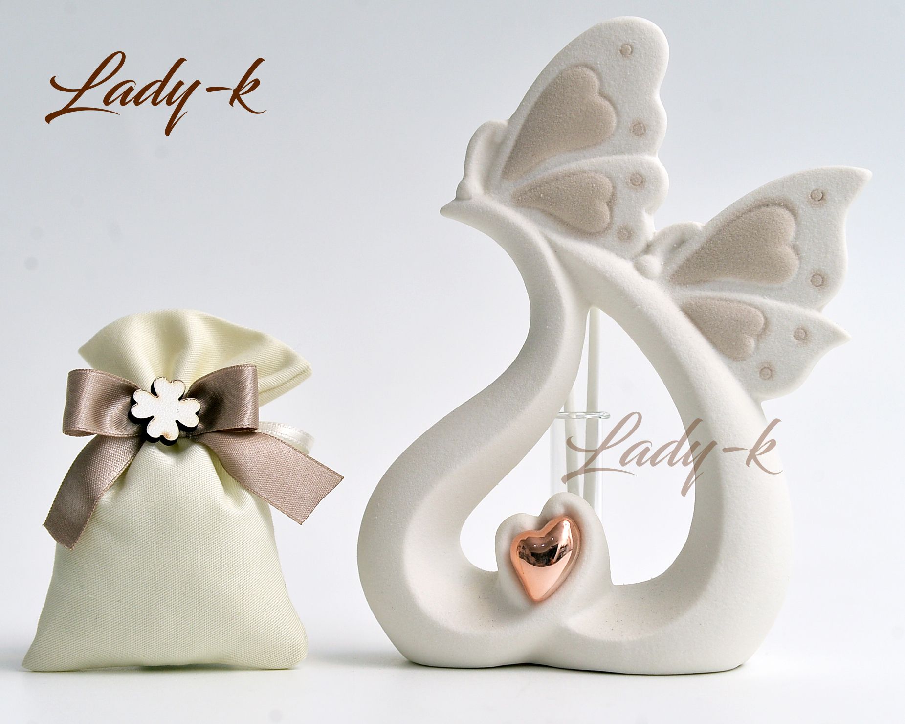 Statuina in ceramica color crema con ali di farfalla e cuore dorato, accanto a una piccola borsa di stoffa beige legata con un nastro.