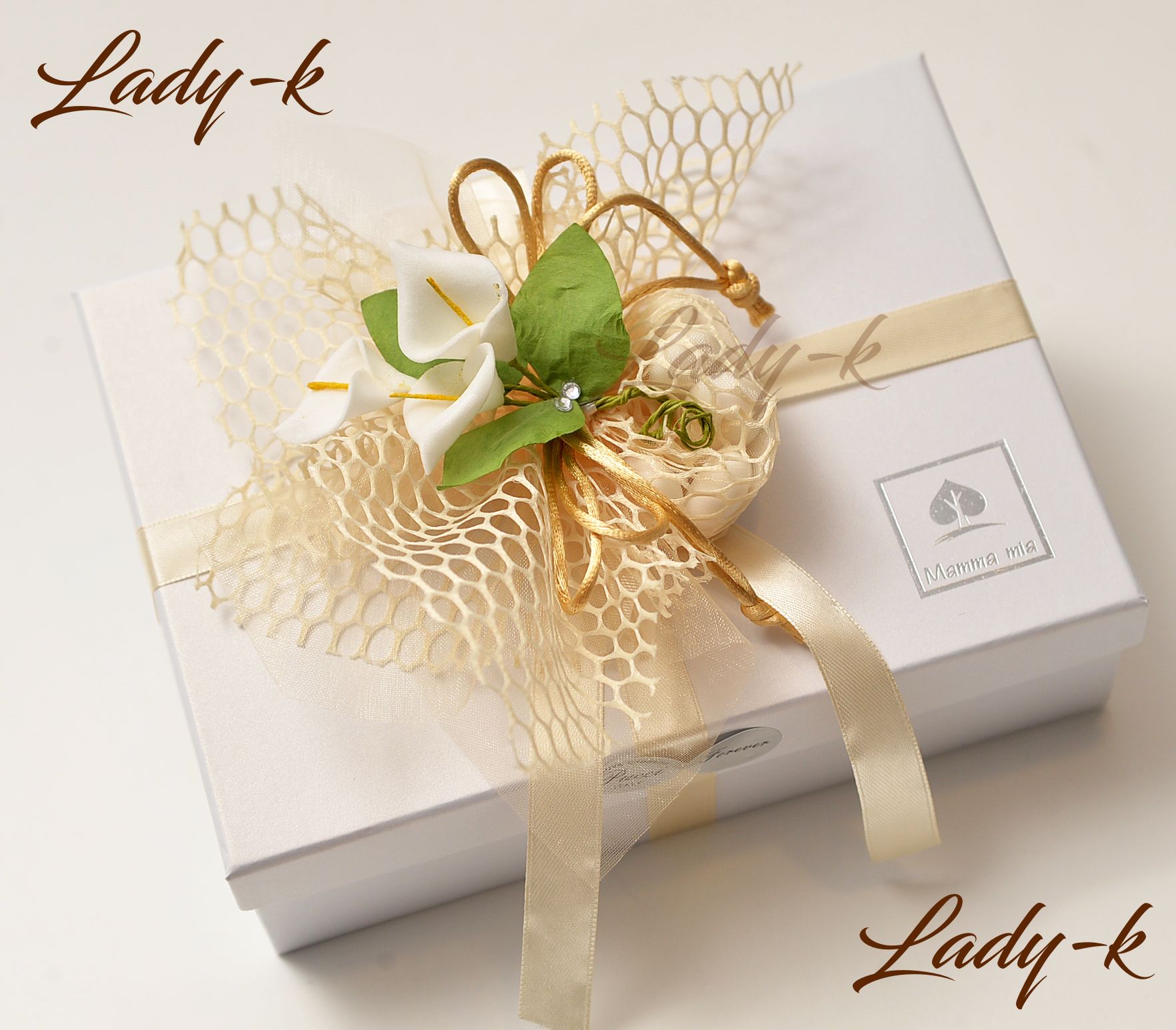 Scatola regalo bianca legata con un nastro color crema e decorata con dettagli floreali e in rete.