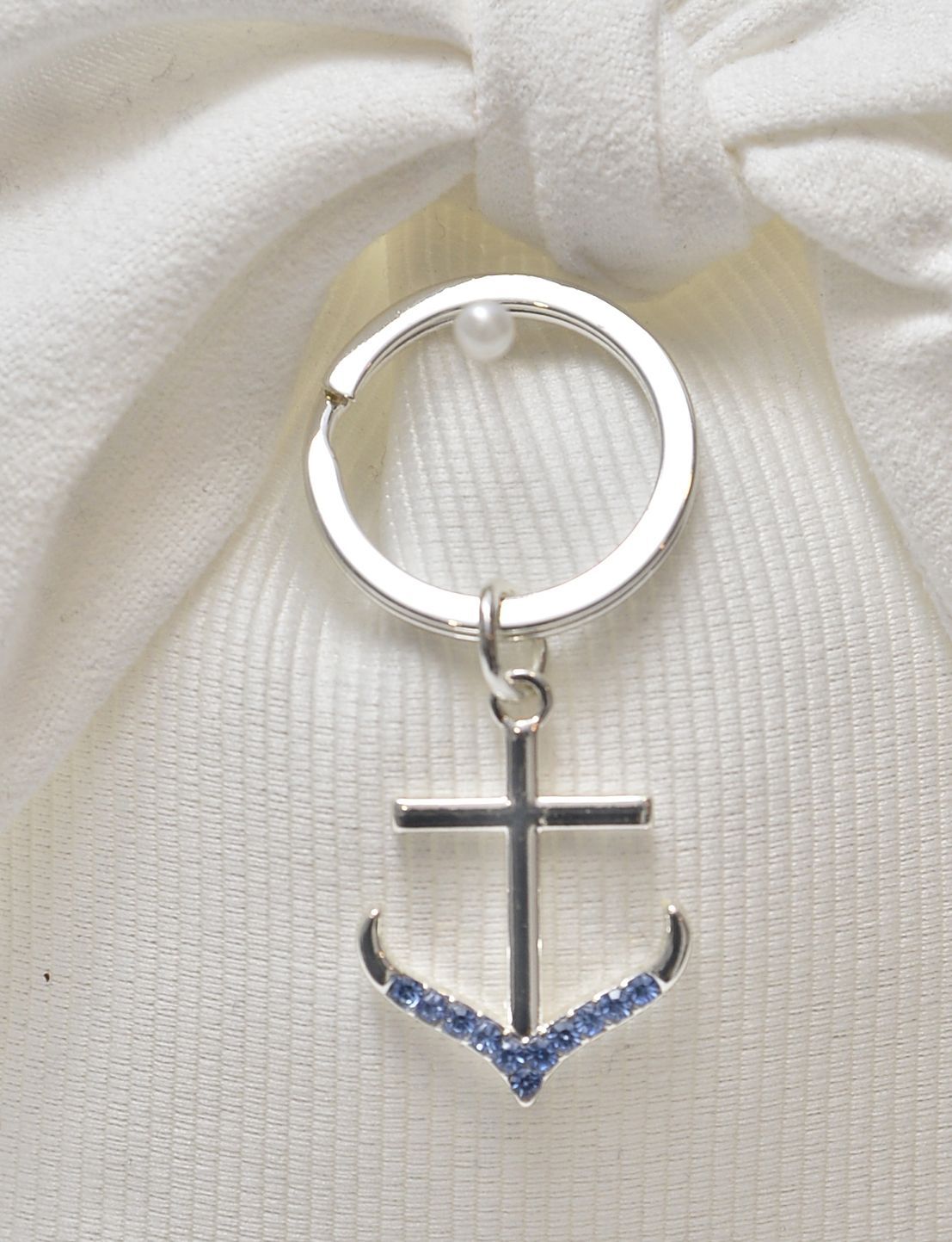 Portachiavi a forma di ancora argentata con dettagli blu, appeso a un tessuto bianco.