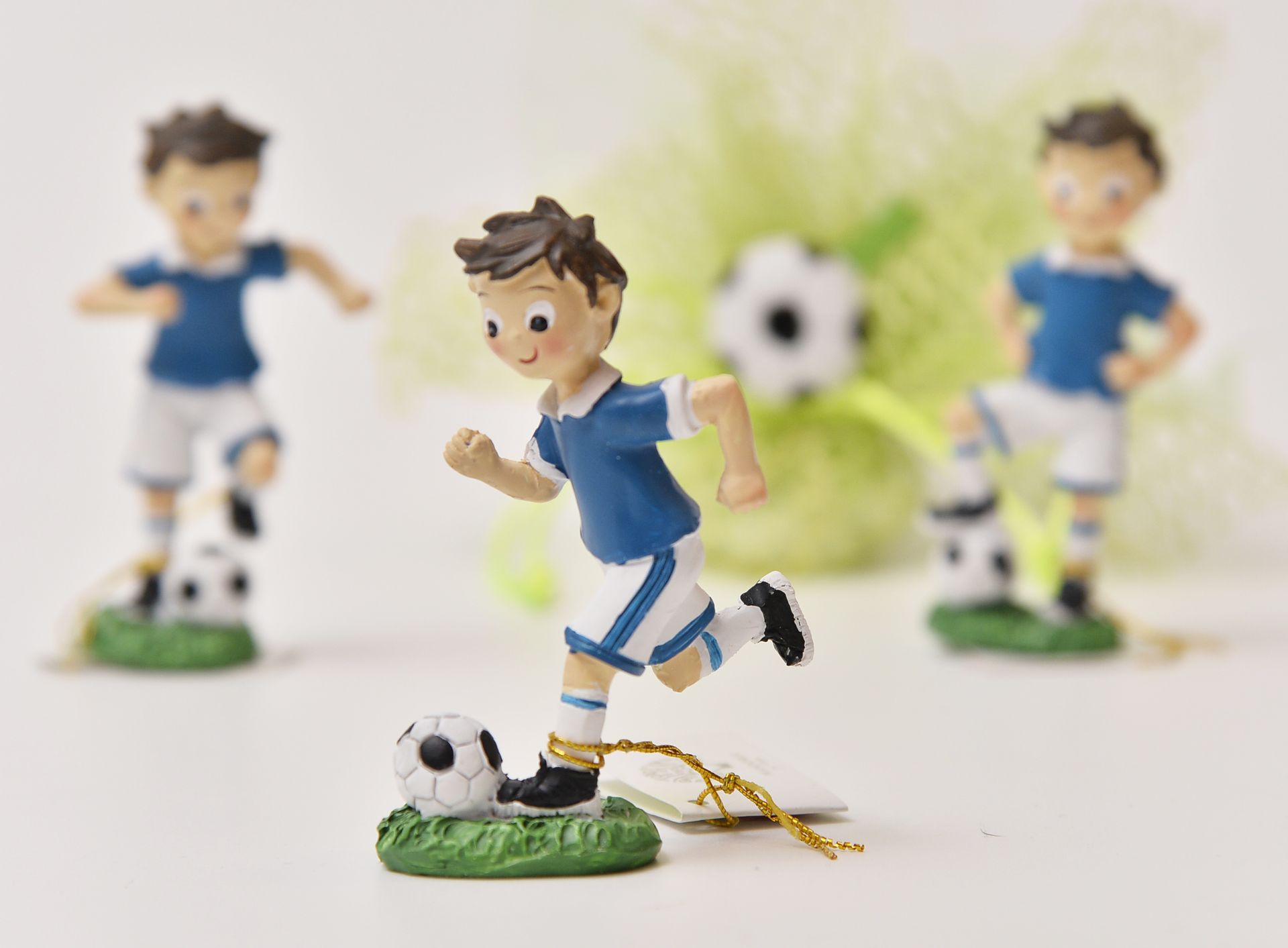 Tre statuette di calciatori, una delle quali corre verso lo spettatore, le altre due sono in posa con palloni da calcio; tutte indossano uniformi blu e bianche.