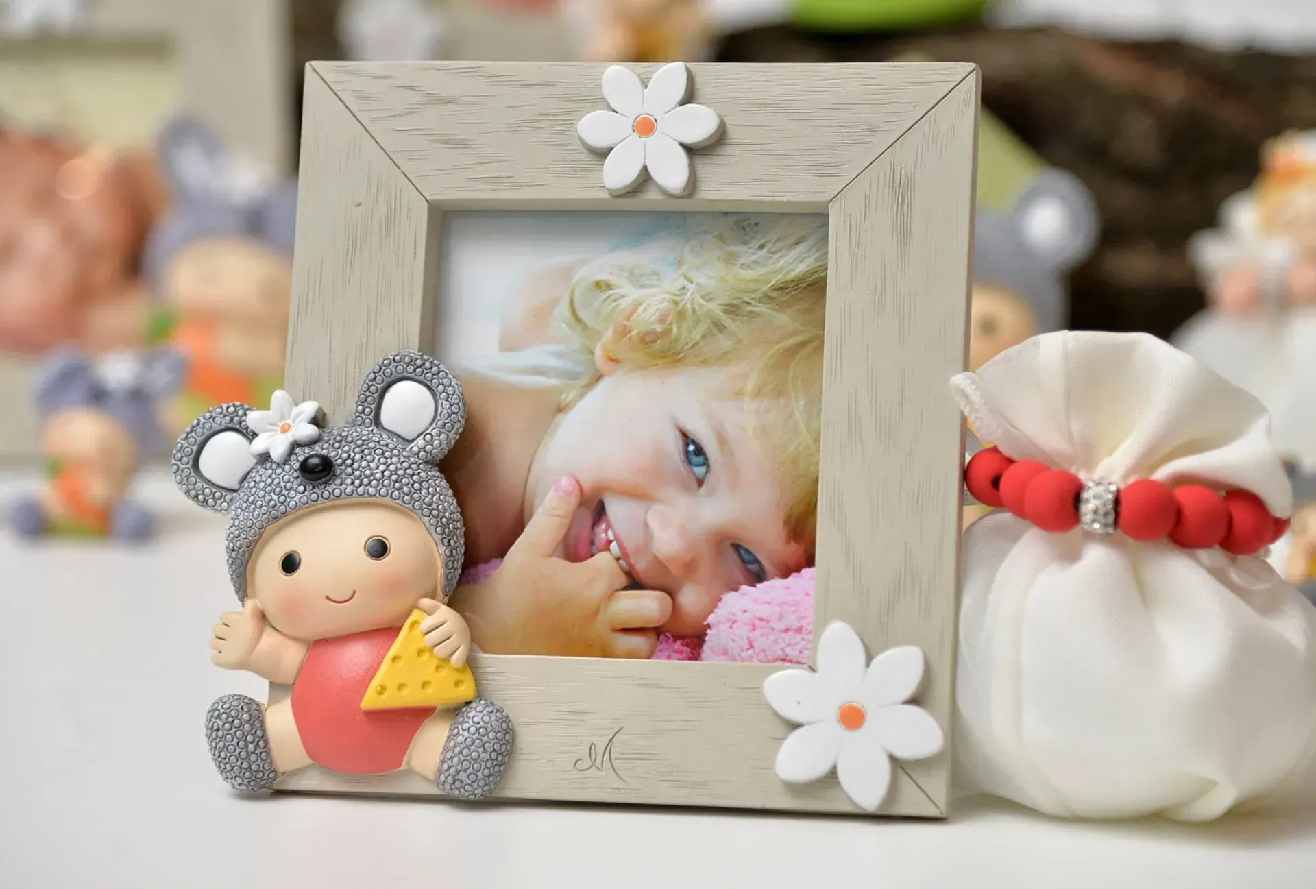 Foto di un bambino in una cornice decorata con un topolino; colori tenui, bomboniere sullo sfondo.