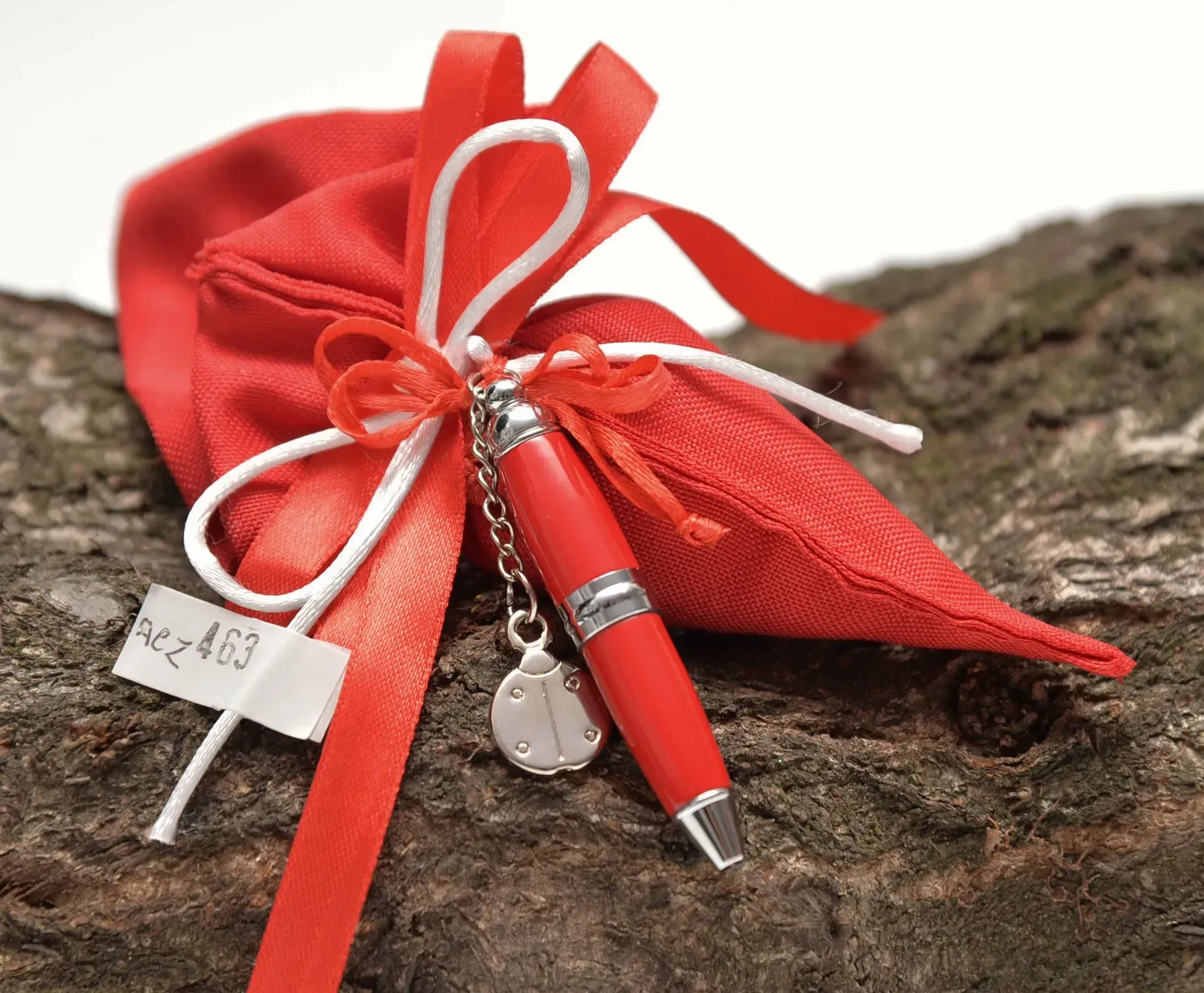 Sacchetto regalo rosso con una penna rossa e un nastro bianco, su una superficie di legno.