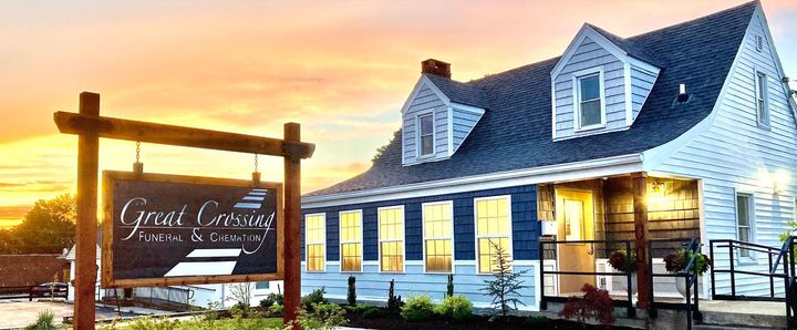 Sunlit white inn with a porch sign at sunset, warmly lit windows, and a coastal-style roof