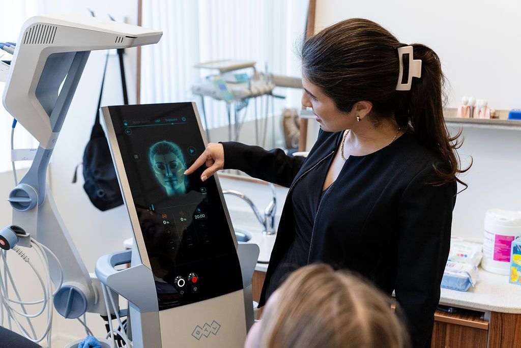 Dentist examining a reclining patient beside a dental monitor in a bright clinic