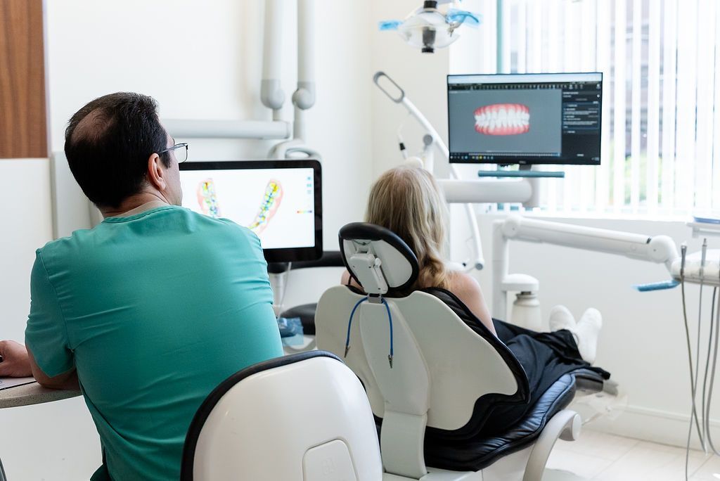 Two people seated in a dental clinic, viewing X-ray images on monitors