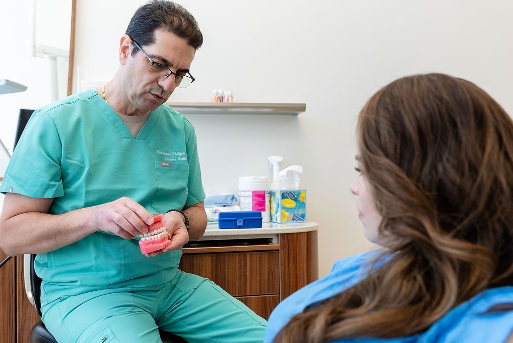 Doctor in green scrubs talks with a seated patient in a clinic exam room.