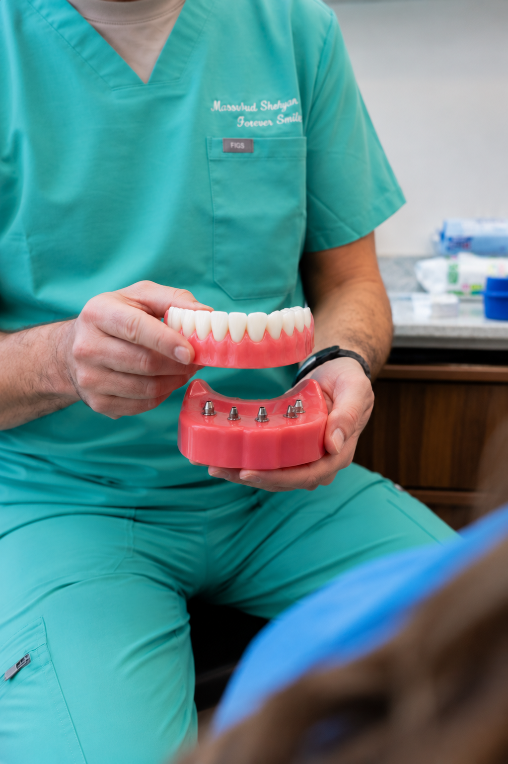 Dentist in teal scrubs showing dentures in a dental office