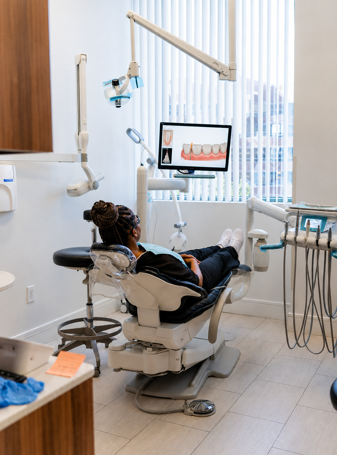 Dental patient reclined in a chair during a checkup, with a monitor and dentist tools in a bright clinic.