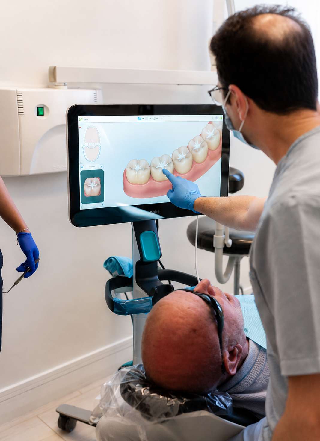 Dentist explaining 3D tooth scan on a large monitor to a patient in a dental chair