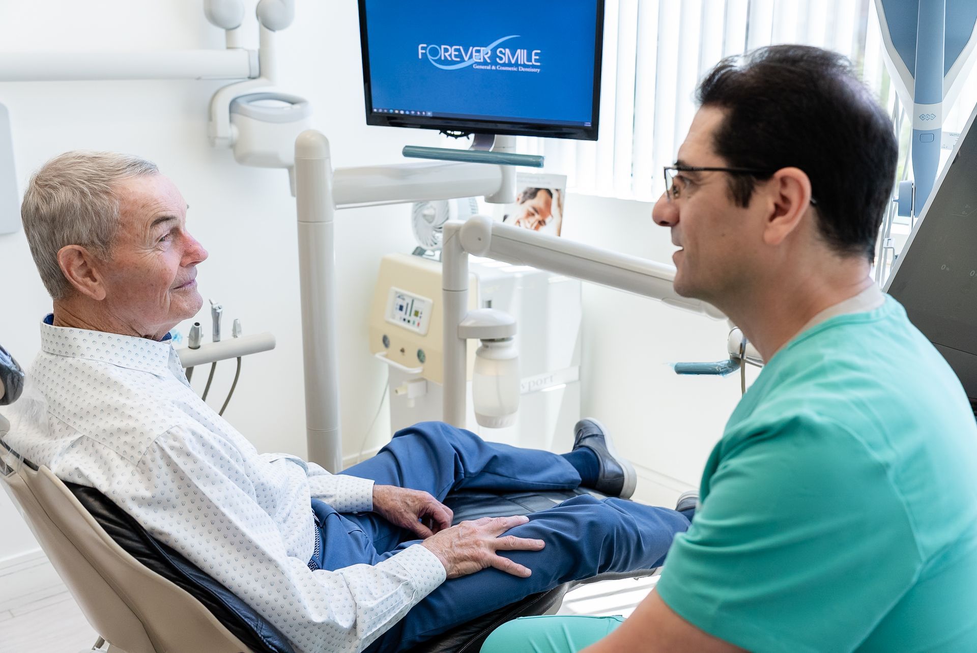 Patient and clinician talking in a hospital room, with a monitor above the bed.