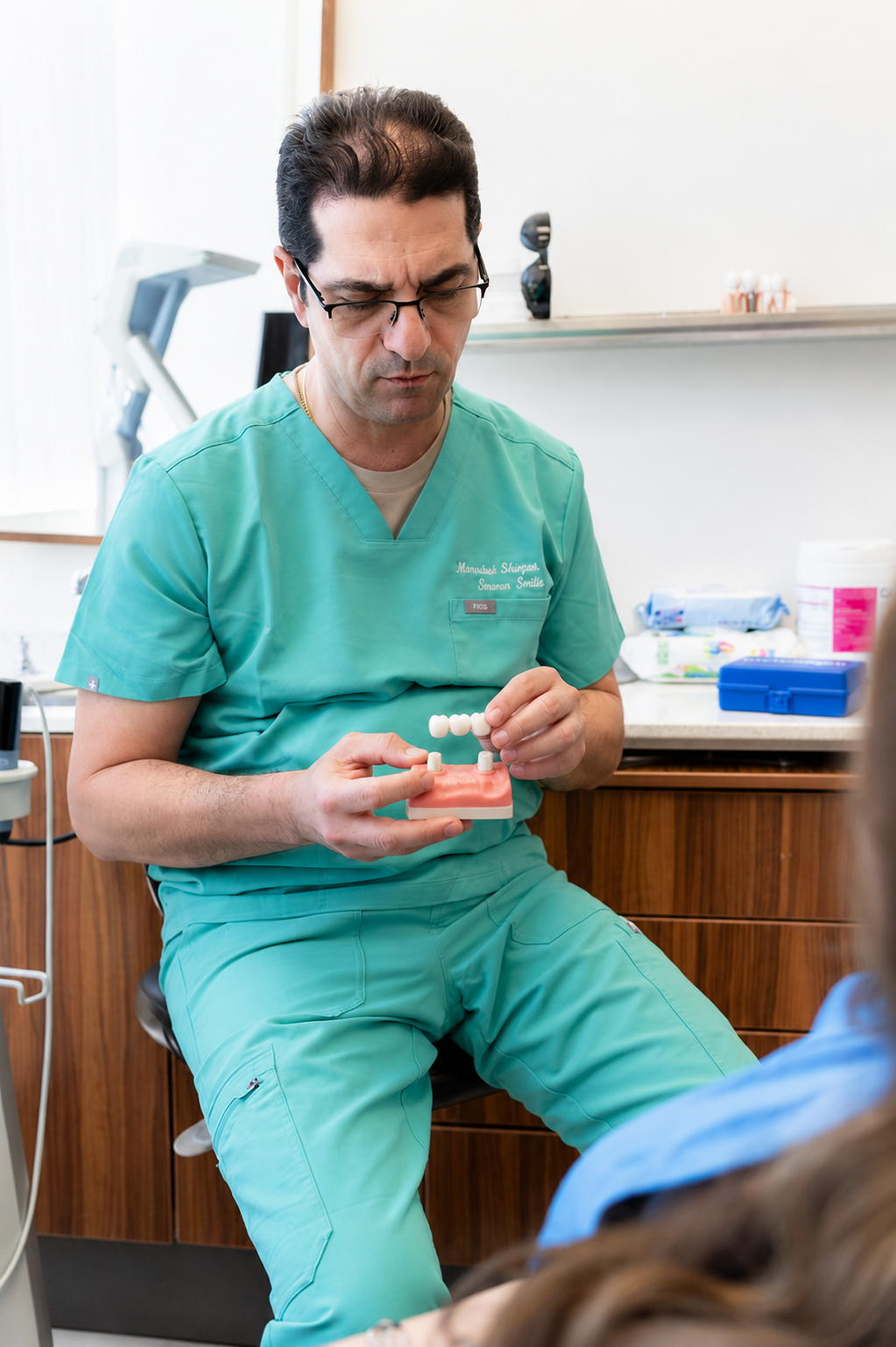 Doctor in teal scrubs holding a syringe in a clinic room