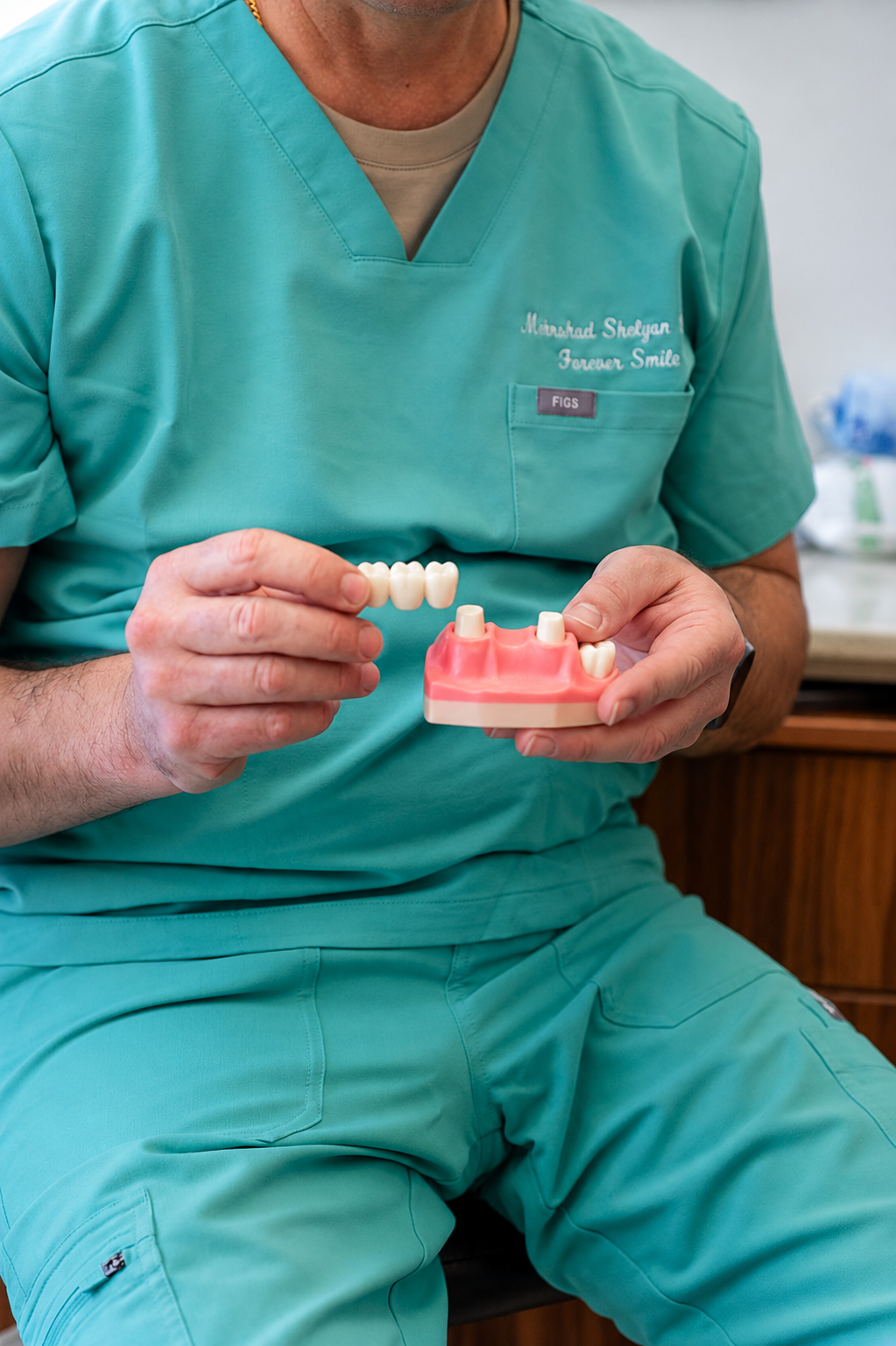 Dentist in teal scrubs holding a dental model and toothbrush in a clinic
