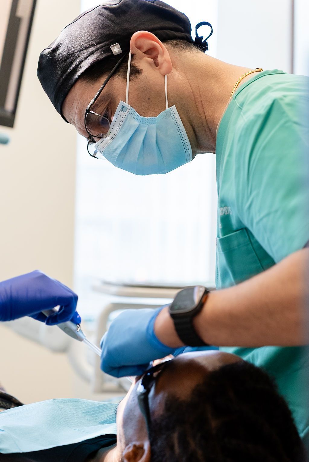 Dentist in green scrubs and mask working on a patient during a dental procedure