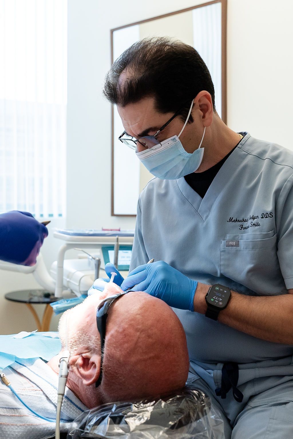 Dentist in scrubs and mask treating a patient in a dental chair