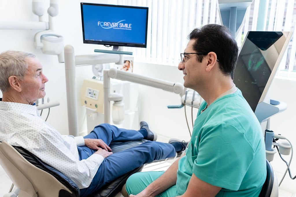 Dentist examining a patient in a bright dental clinic while a monitor displays an x-ray.