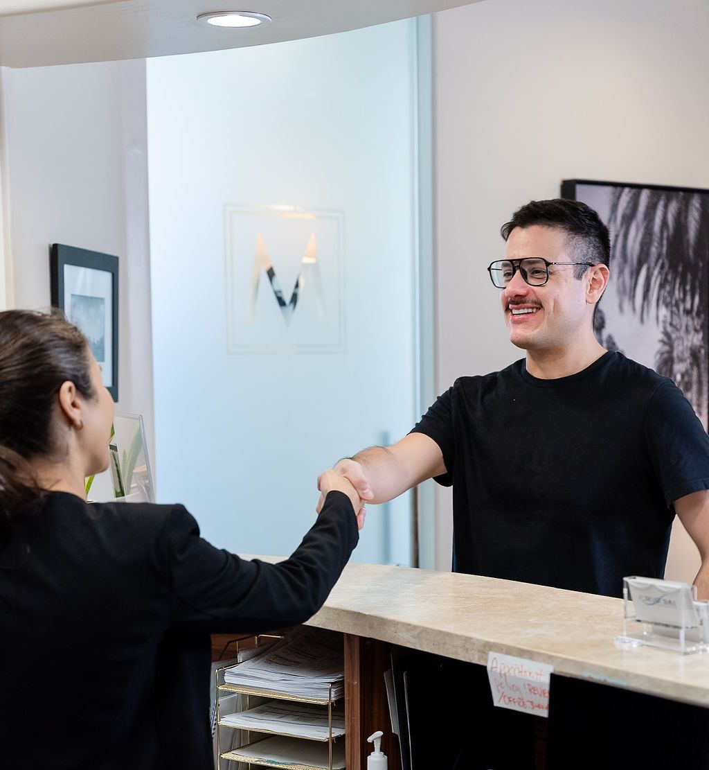 Two people shaking hands across a reception desk in a bright office lobby
