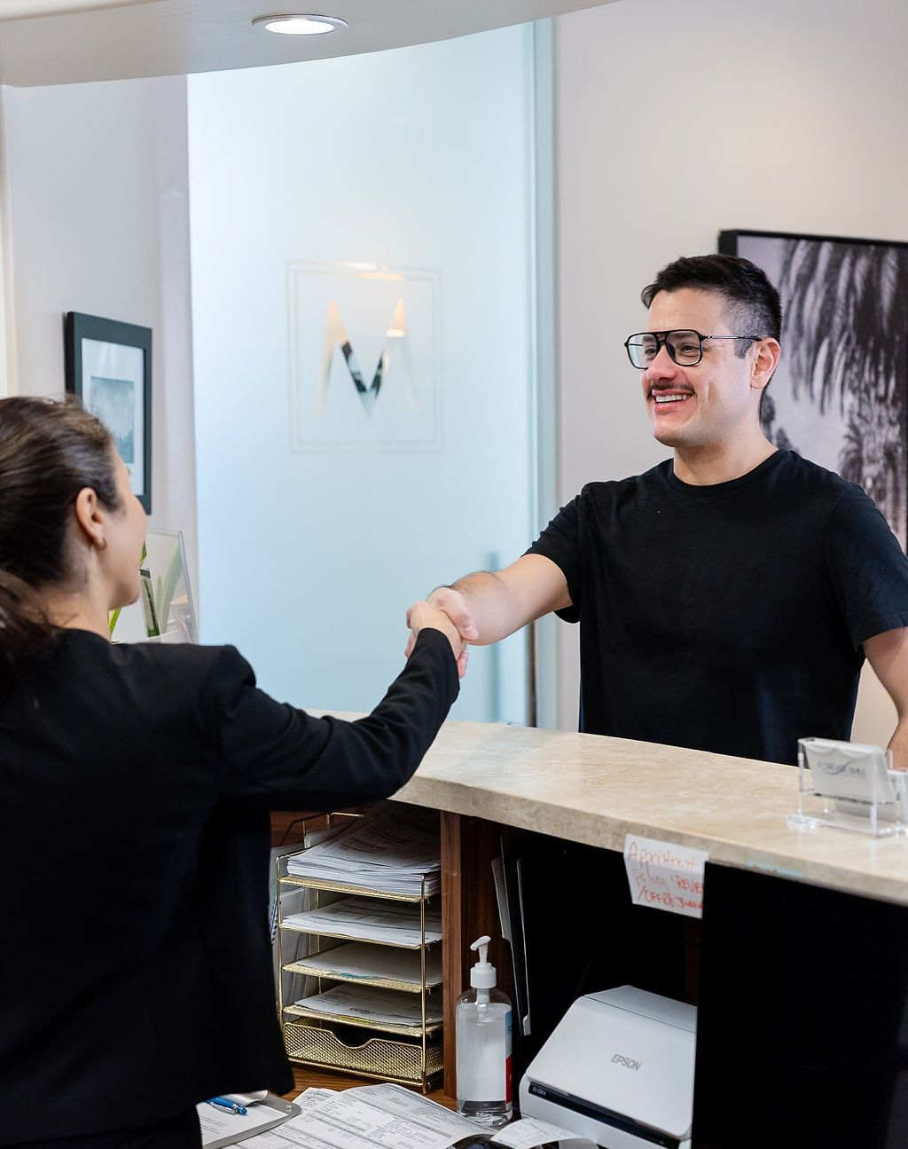 Receptionist shaking hands with a smiling customer at a front desk