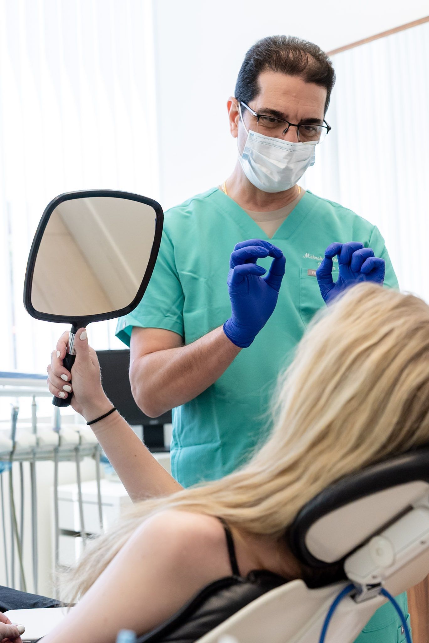 Dr. Shelyan holding a hand mirror so a patient can see her smile