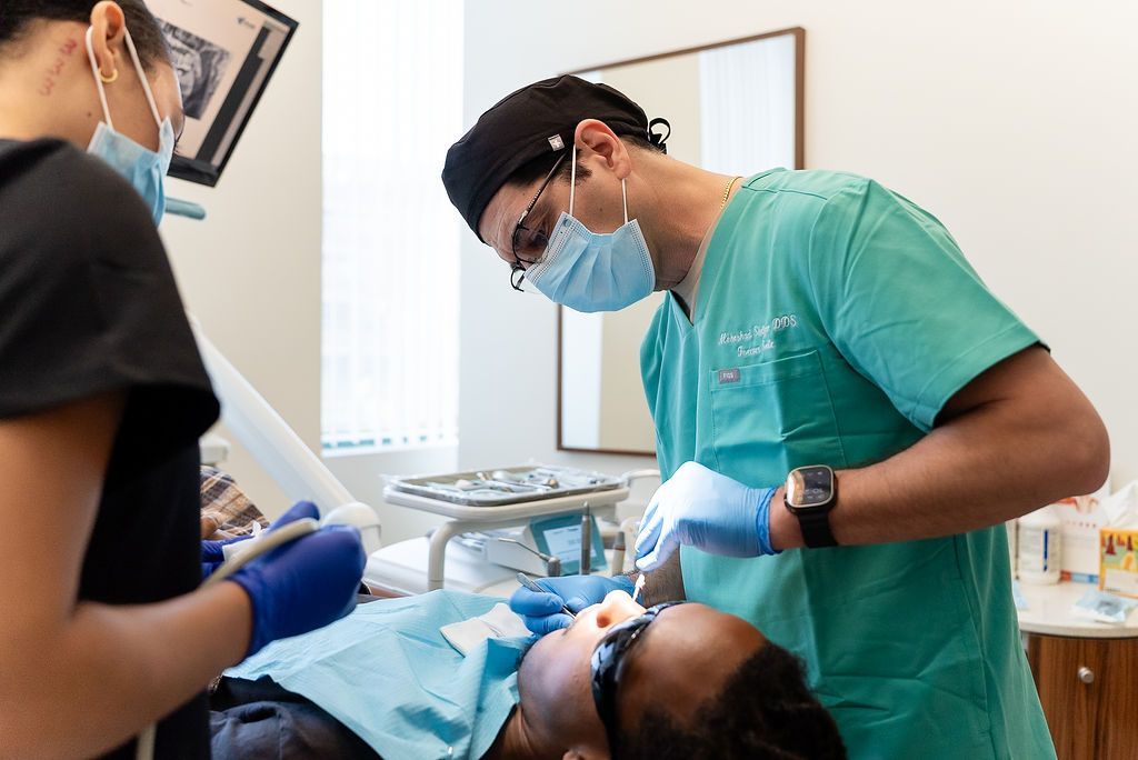 Dentist and assistant treating a patient in a dental clinic, wearing masks and gloves.