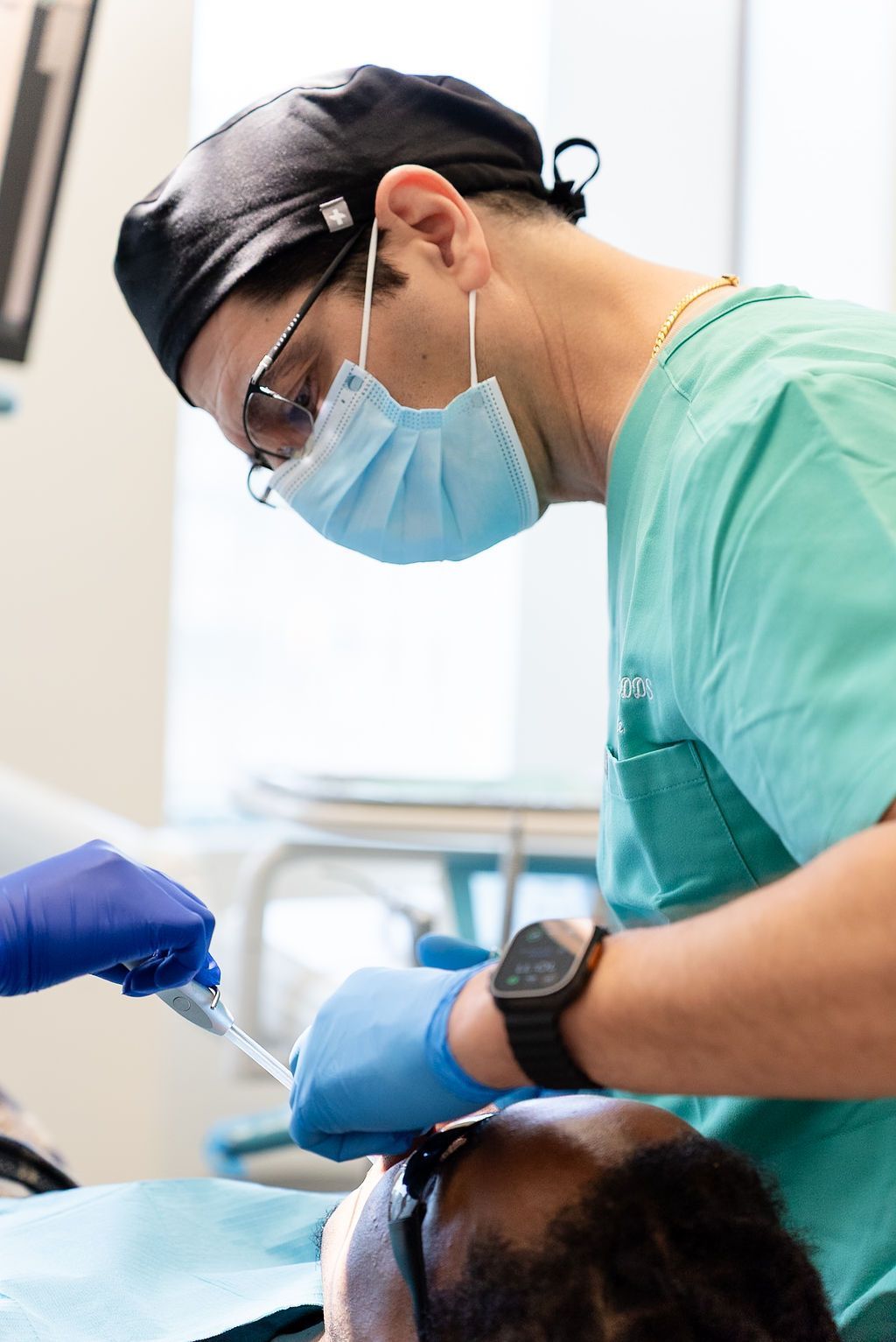 Dentist in green scrubs and blue gloves treating a patient in a dental chair