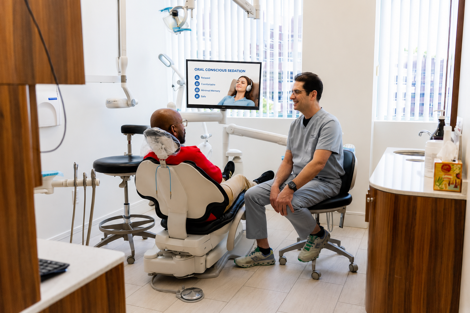 Dentist consulting with a patient in a bright dental office, with a monitor showing x-rays.
